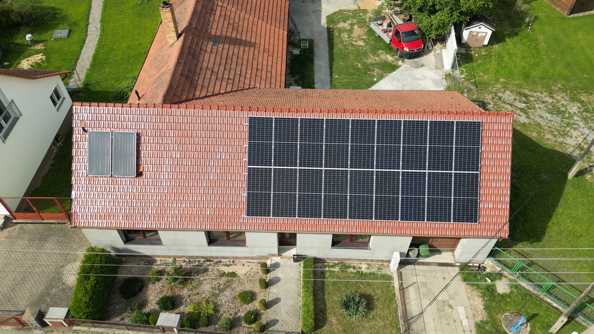 Letecký pohled na rodinný dům s polem fotovoltaických panelů na červené taškové střeše